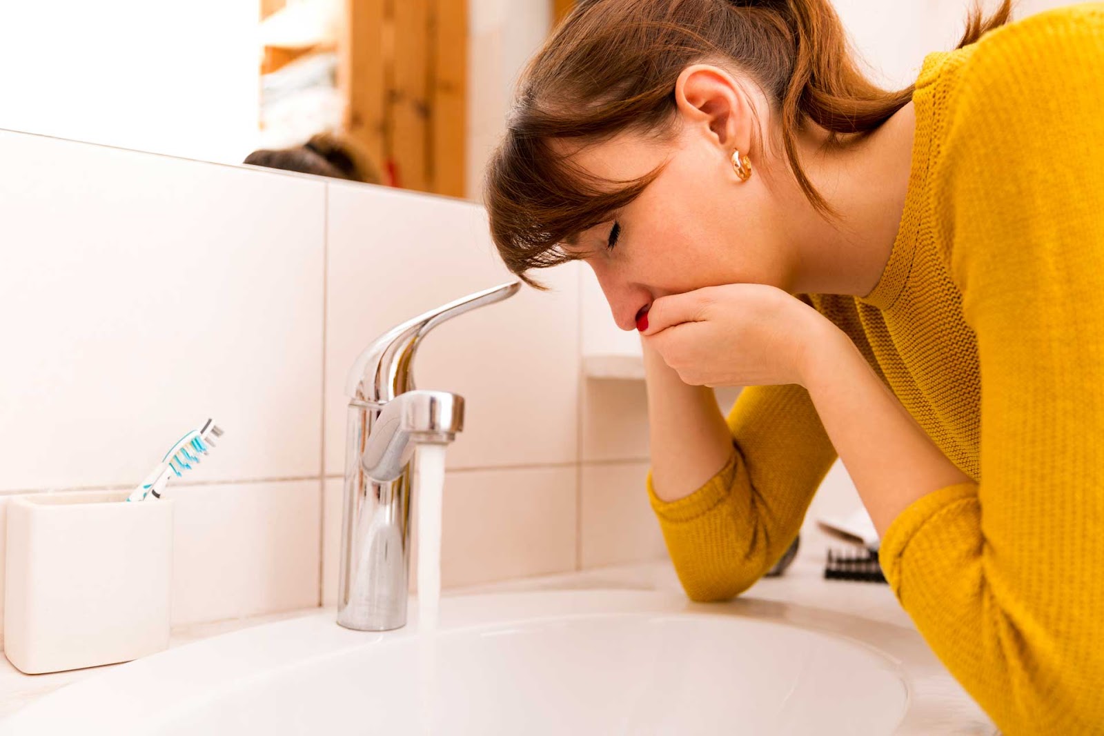 Woman leans over bathroom sink to rinse her mouth, apparently feeling ill.