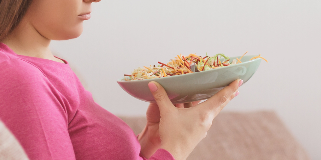 Woman in pink shirt holds a salad and looks at it with disinterest. 