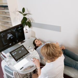 Young woman lays on exam table while sonographer uses the ultrasound wand on her abdomen 
