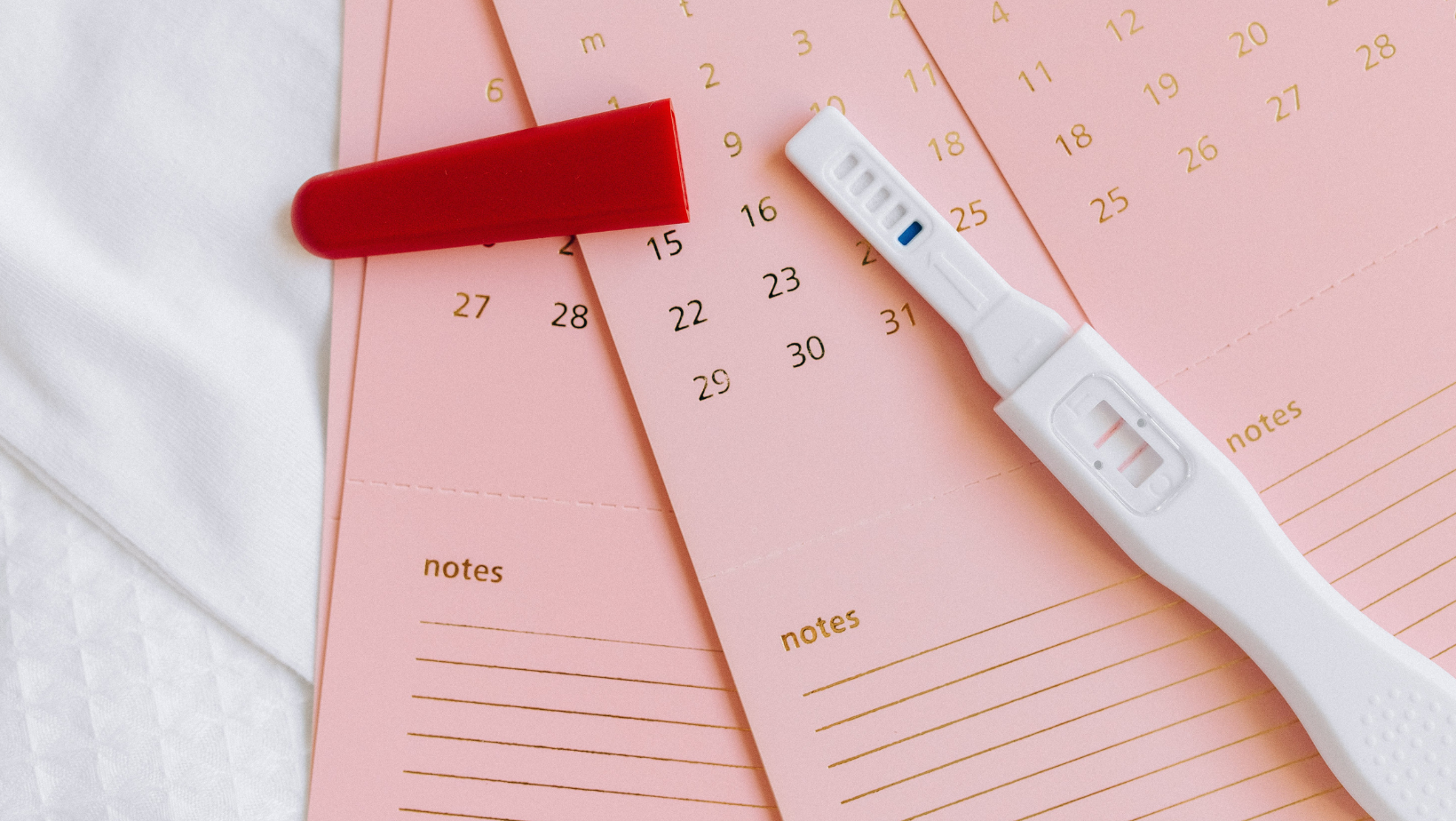 Pregnancy test lays on pink paper calendars