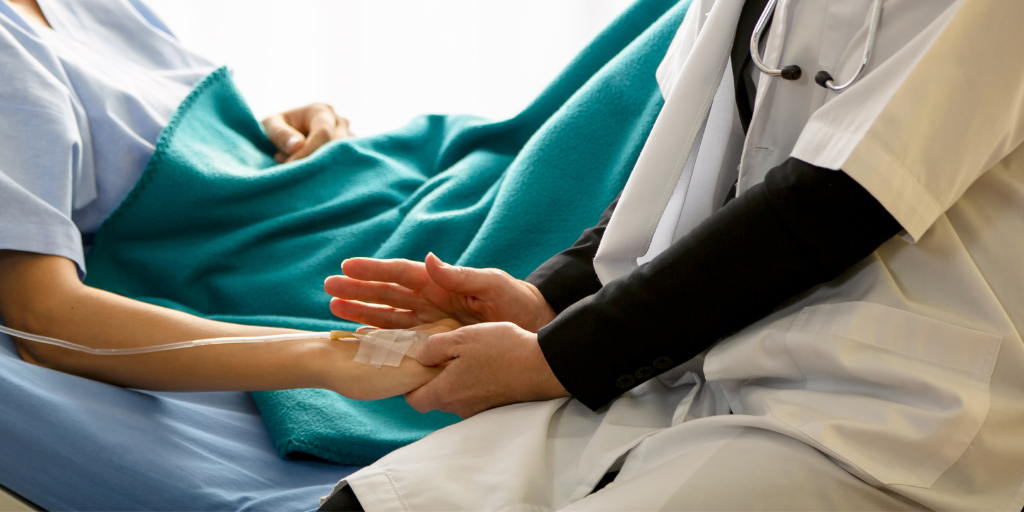 Doctor comforts a woman in a hospital bed, patting her hand