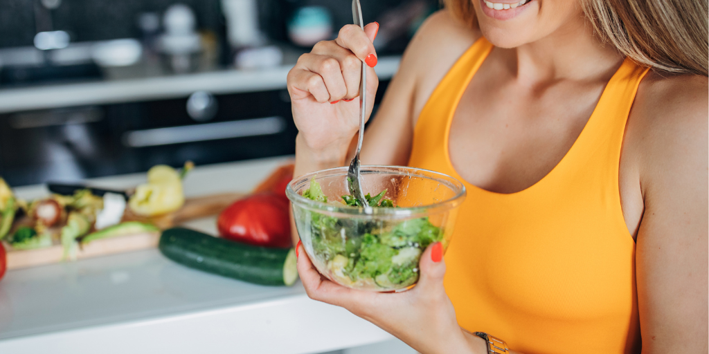 Woman in yellow athletic clothing eats a salad.