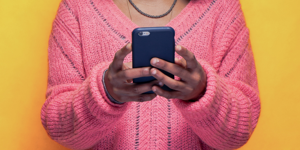 Young woman in pink sweater holds phone in navy phone case in both hands.