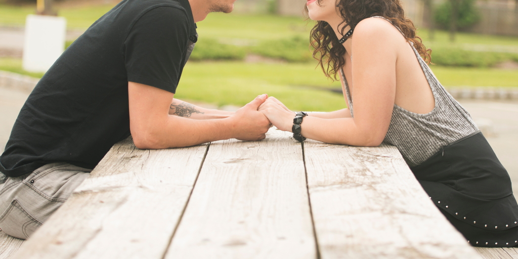 Couple setting across from each other at a picnic table, holding hands